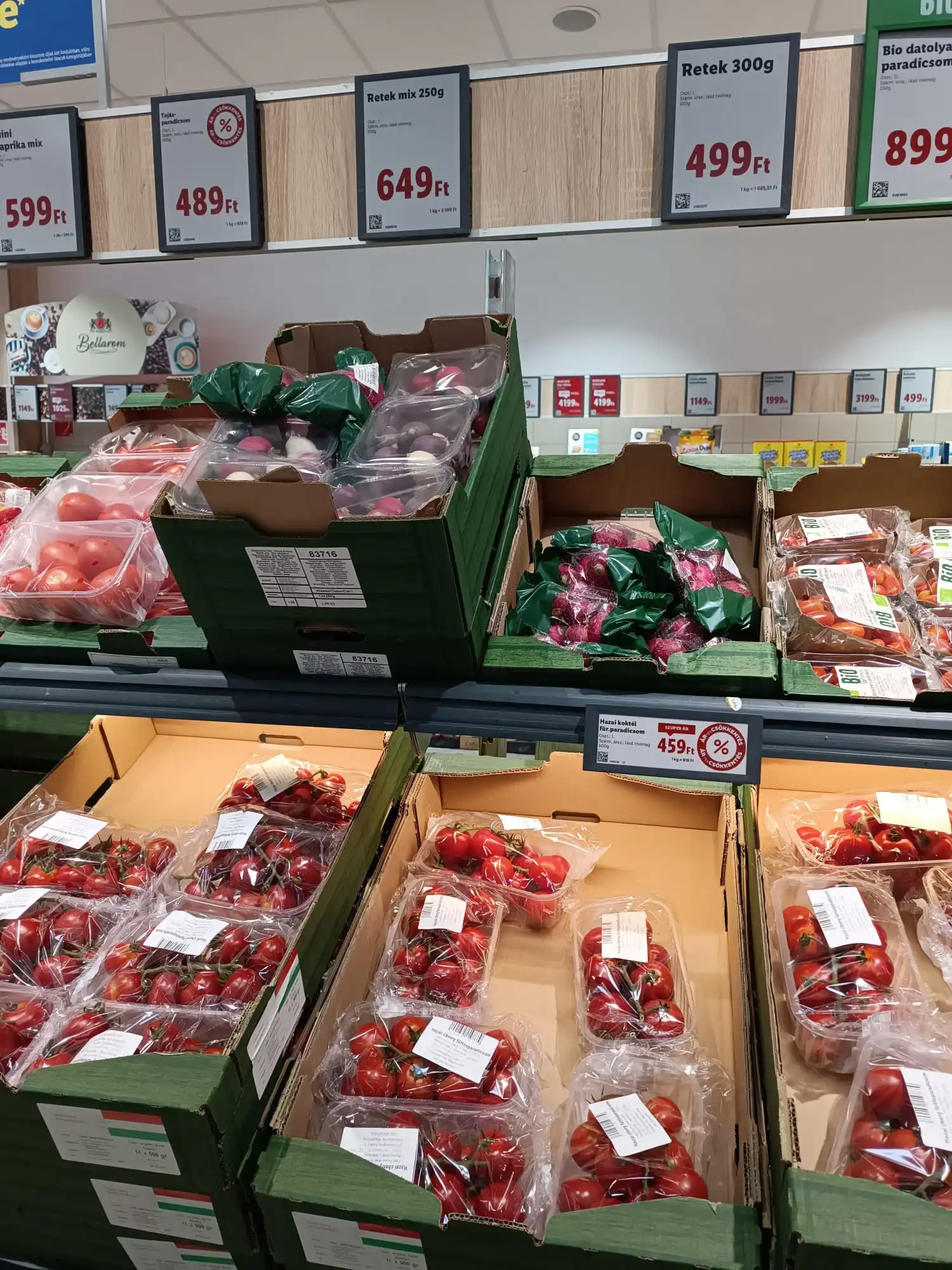 Fresh tomatoes, cherry tomatoes and radishes displayed in a Hungarian supermarket with price signs showing costs in Hungarian Forint (Ft).